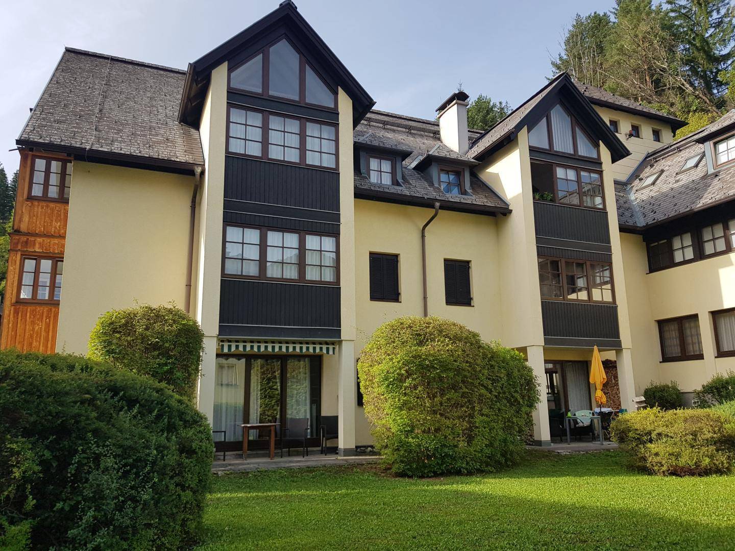 Traditionelles Gebäude im alpinen Stil mit mehreren Etagen, Giebeldächern und gepflegter Grünfläche.