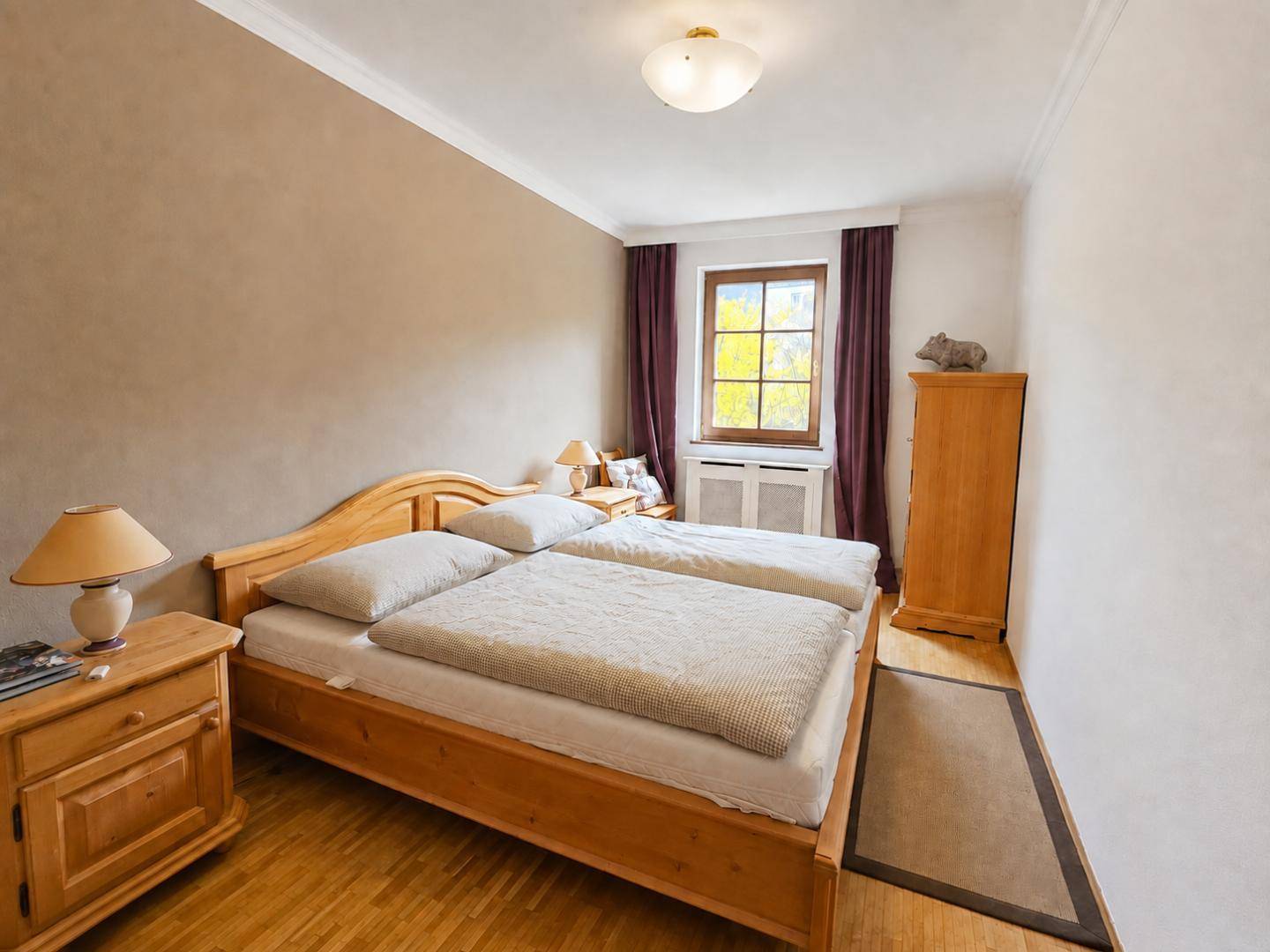 Helles Schlafzimmer mit zwei Einzelbetten, Holzmöbeln und einem Fenster mit Blick ins Grüne.