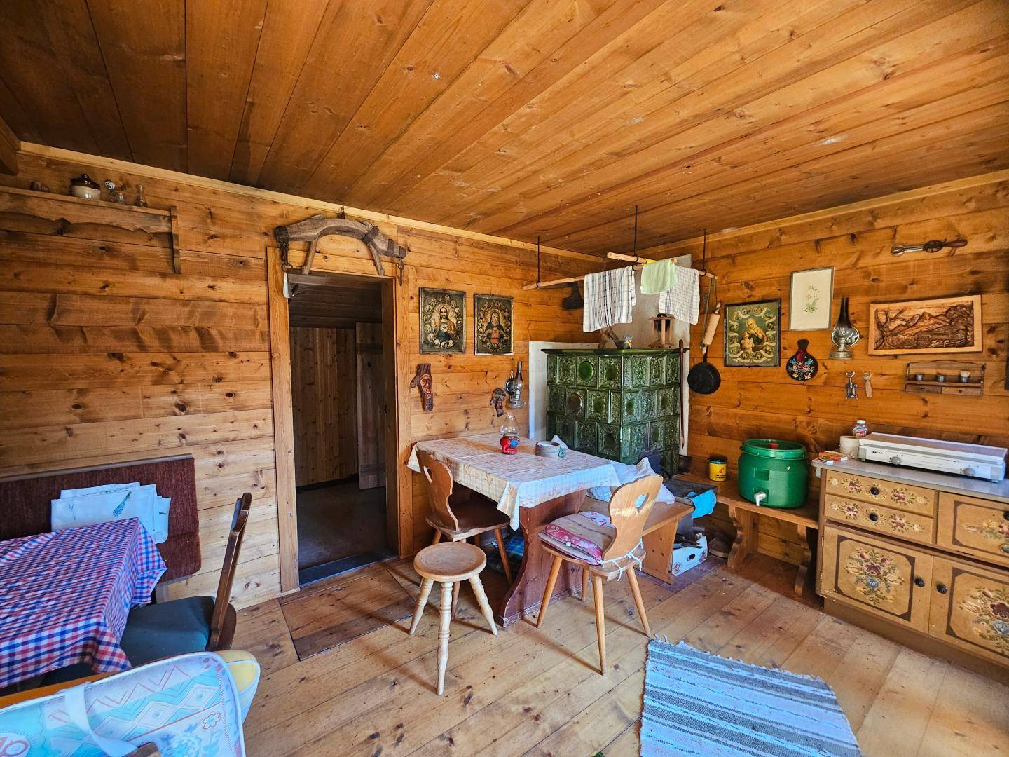Gemütlicher Wohn- und Essbereich in einer Holzhütte mit traditionellem Kachelofen und Holzwänden.