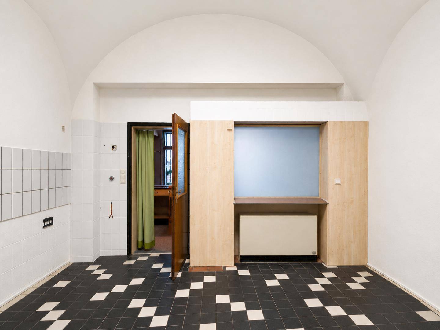 Raum mit gewölbter Decke, schwarz-weißem Fliesenboden und einer Holztrennwand mit Fensteröffnung.