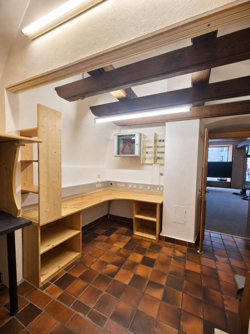 Funktionaler Büroraum mit sichtbaren Holzbalken, eingebautem Schreibtisch und Terrakotta-Fliesenboden.