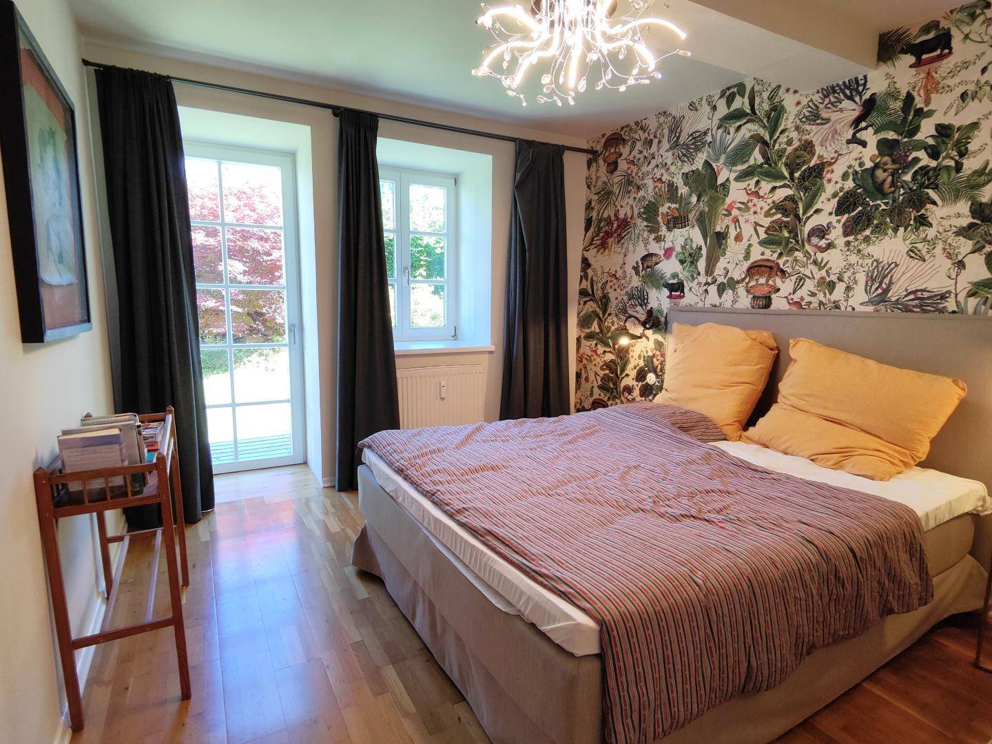 Schlafzimmer mit Holzboden, auffälliger Tapete und Zugang zu einem Außenbereich.