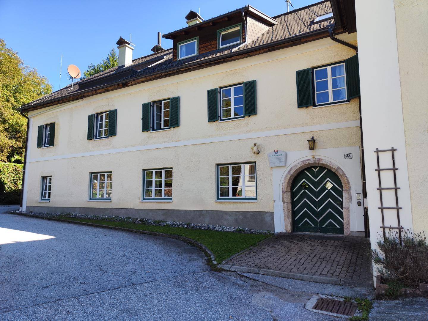 Historisches Gebäude mit gelber Fassade, grünen Fensterläden und markantem Eingangstor.