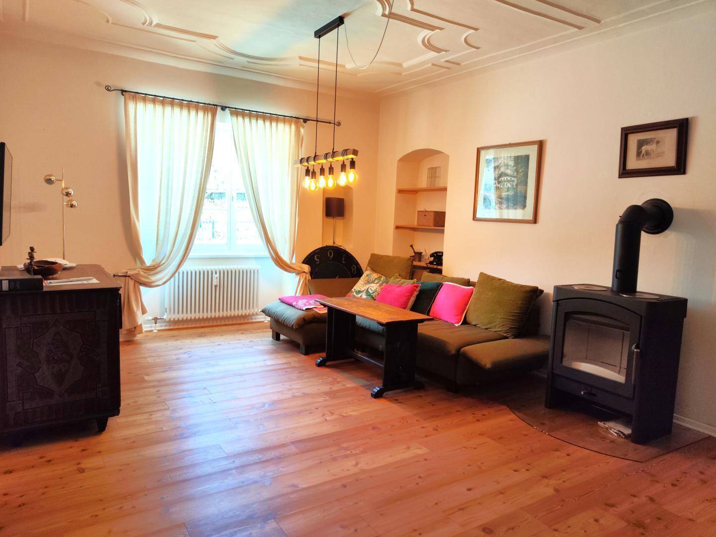 Gemütliches Wohnzimmer mit Holzboden, Stuckdecke, Kaminofen und bequemer Sitzecke.
