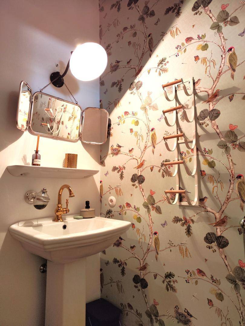 Charmantes Gäste-WC mit floraler Tapete, Einzelwaschbecken und goldenen Armaturen.