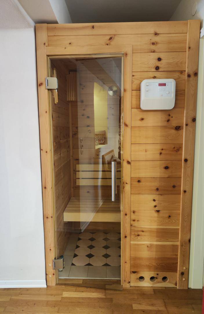 Moderne Holzsauna mit Glastür und Steuerungselementen für entspannende Momente.