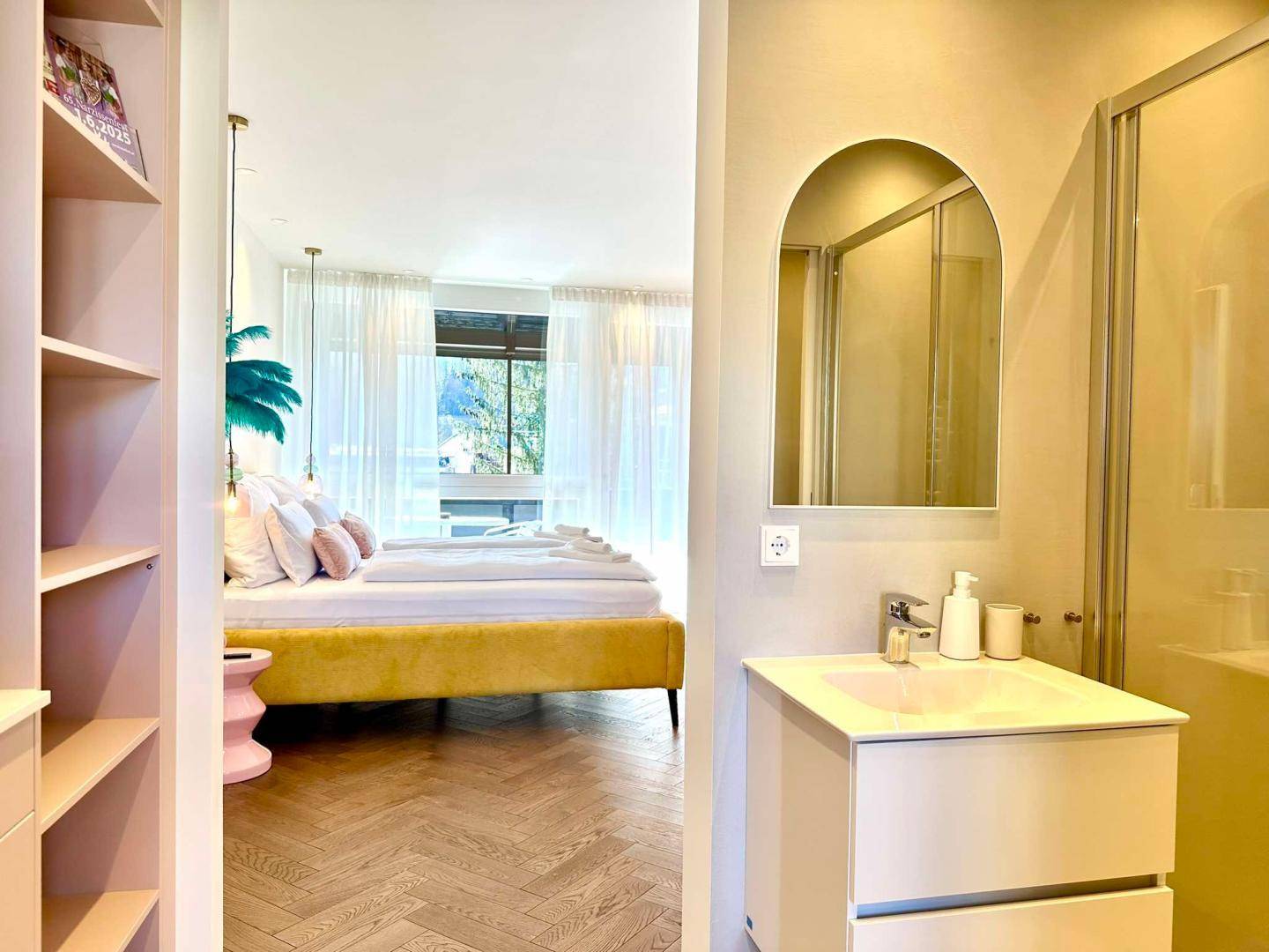Blick vom Badezimmer in das angrenzende Schlafzimmer mit gelbem Bett und Holzboden.