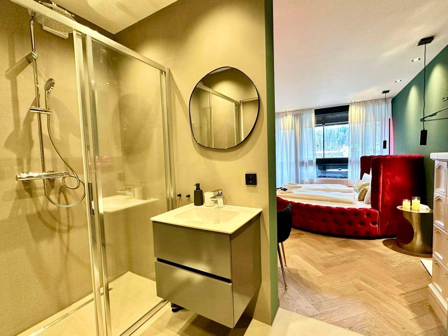 Badezimmer mit Duschkabine und Waschbecken, offen zum Schlafbereich mit rotem Bett.