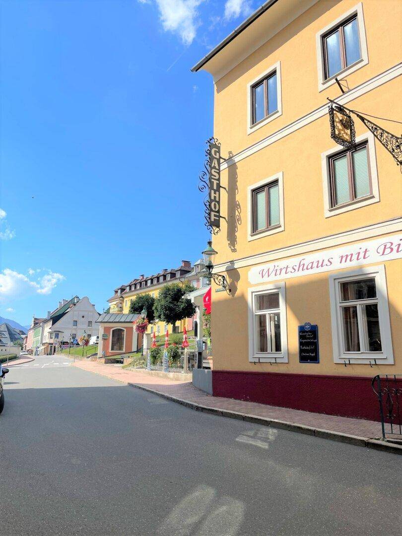 Historisches Gebäude mit gelber Fassade und traditionellem Gasthof-Schild an einer sonnigen Straße.