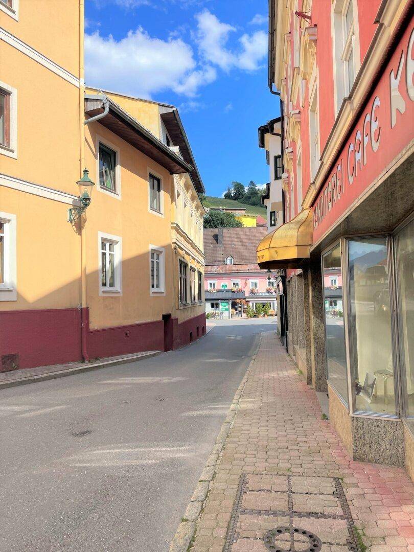 Enge Gasse mit historischen Gebäuden und Geschäften unter blauem Himmel in einer Stadt.