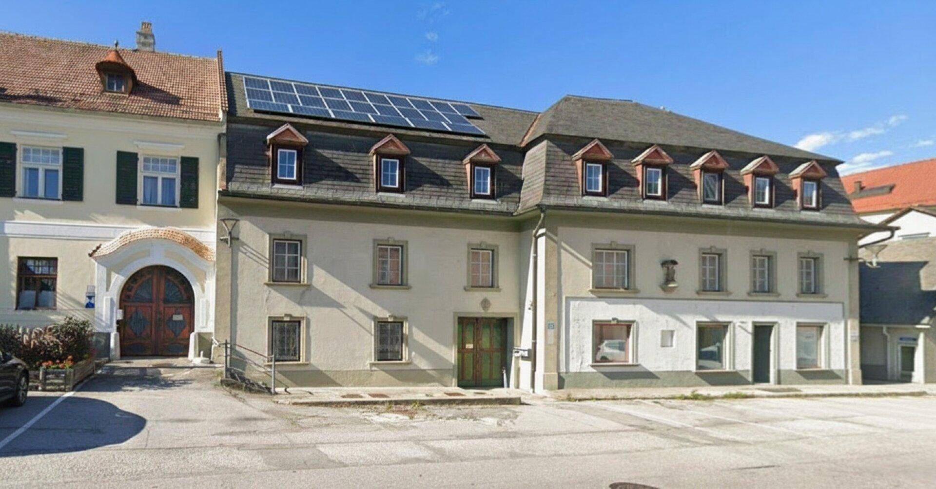 Historisches Gebäude mit Solaranlage auf dem Dach und traditionellen Fenstern in ländlicher Umgebung.