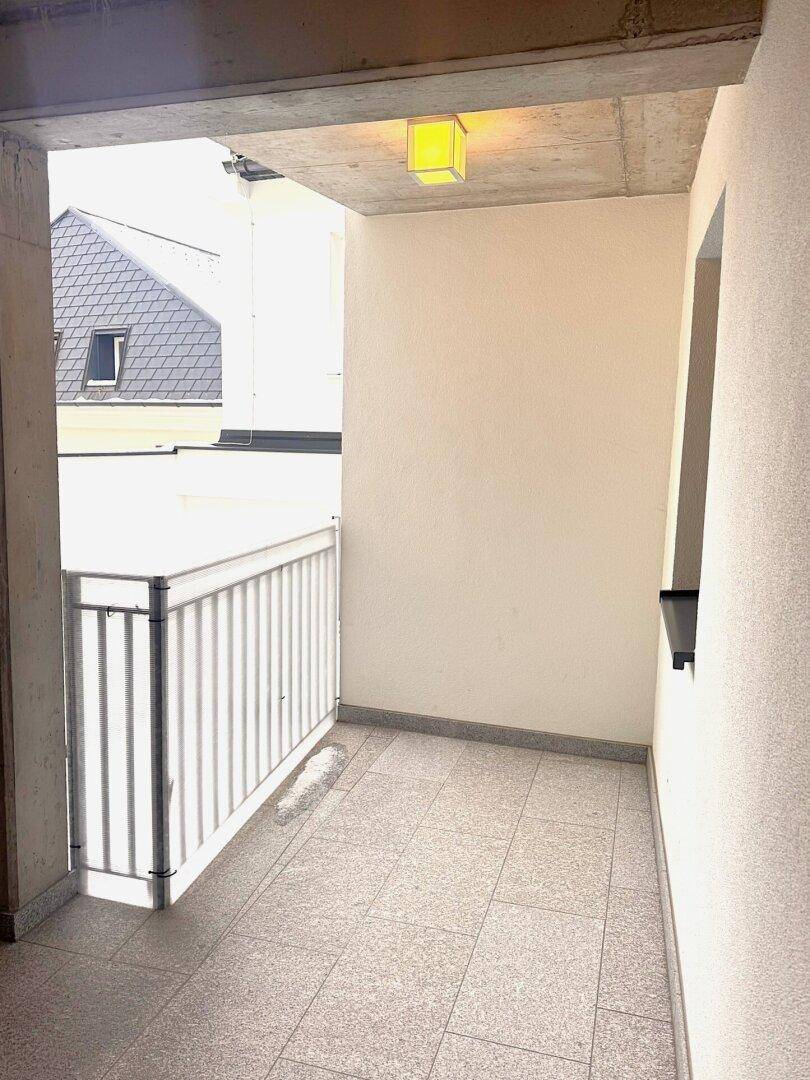 Kleiner Balkon mit Fliesenboden und einem Geländer, bietet einen Blick auf die umliegenden Dächer.