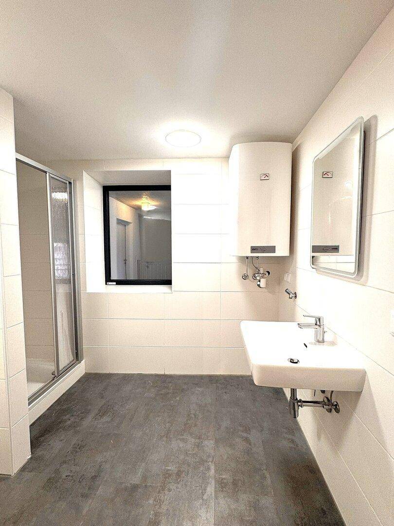 Modernes Badezimmer mit Waschbecken, Duschkabine, weißen Fliesen und einem Fenster.