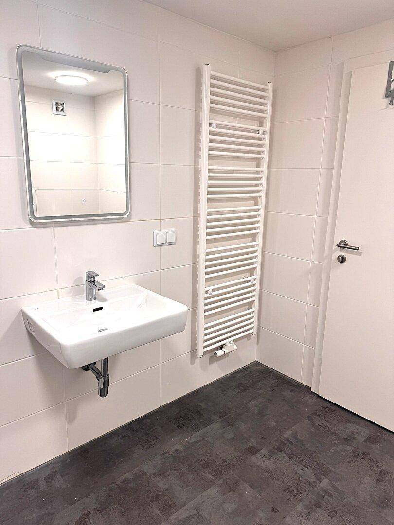 Modernes Badezimmer mit Waschbecken, Spiegel und einem praktischen beheizten Handtuchhalter.