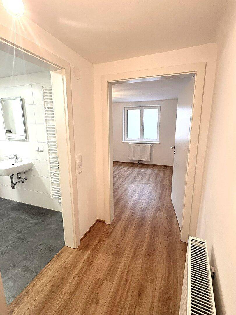 Heller Flur mit Laminatboden, der zu einem Badezimmer und einem weiteren Zimmer führt.