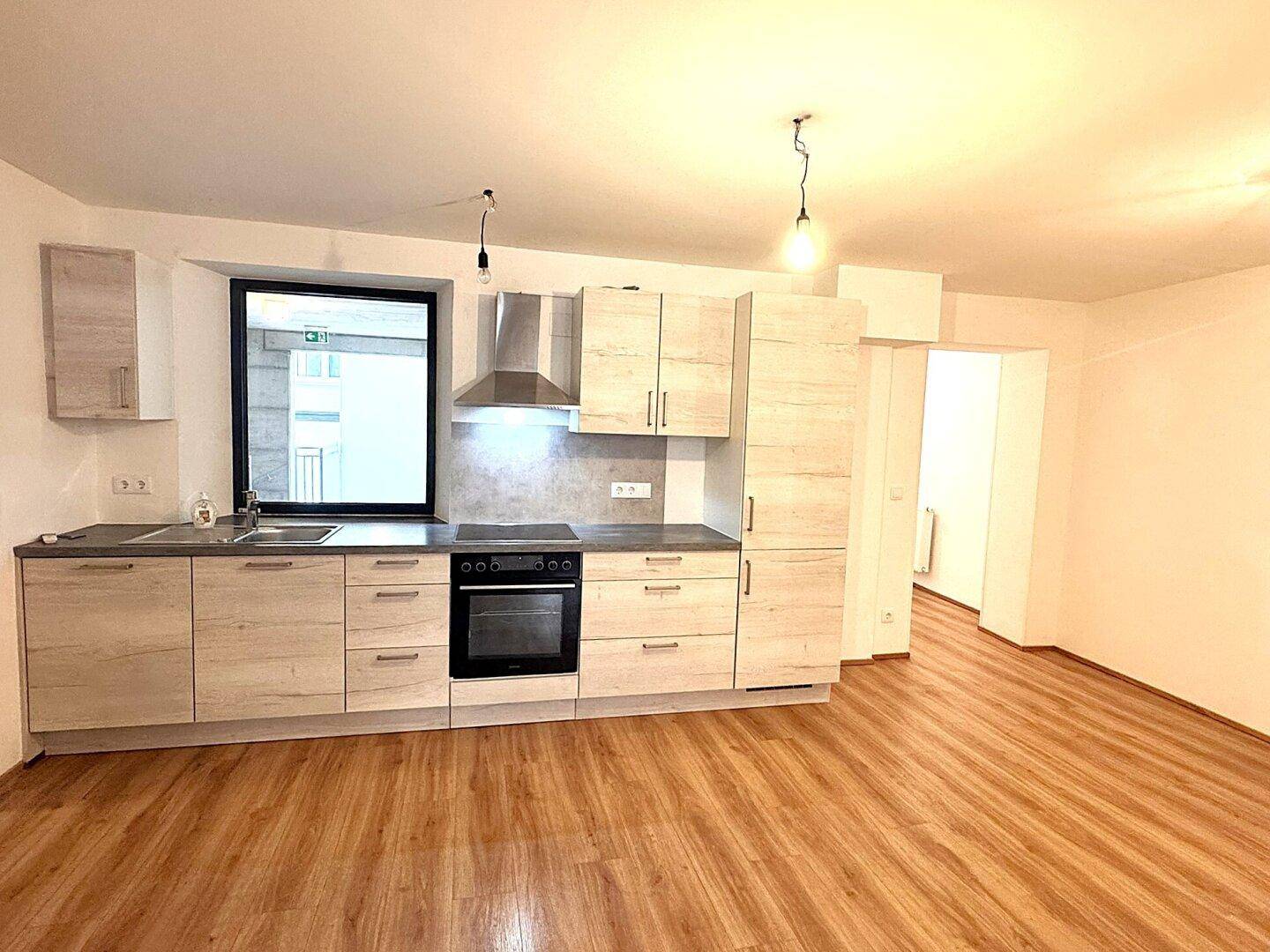 Moderne Einbauküche mit hellen Holzfronten, dunkler Arbeitsplatte und integrierten Geräten.