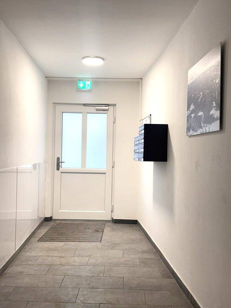 Heller Eingangsbereich des Gebäudes mit Fliesenboden, Briefkästen und einer Eingangstür.