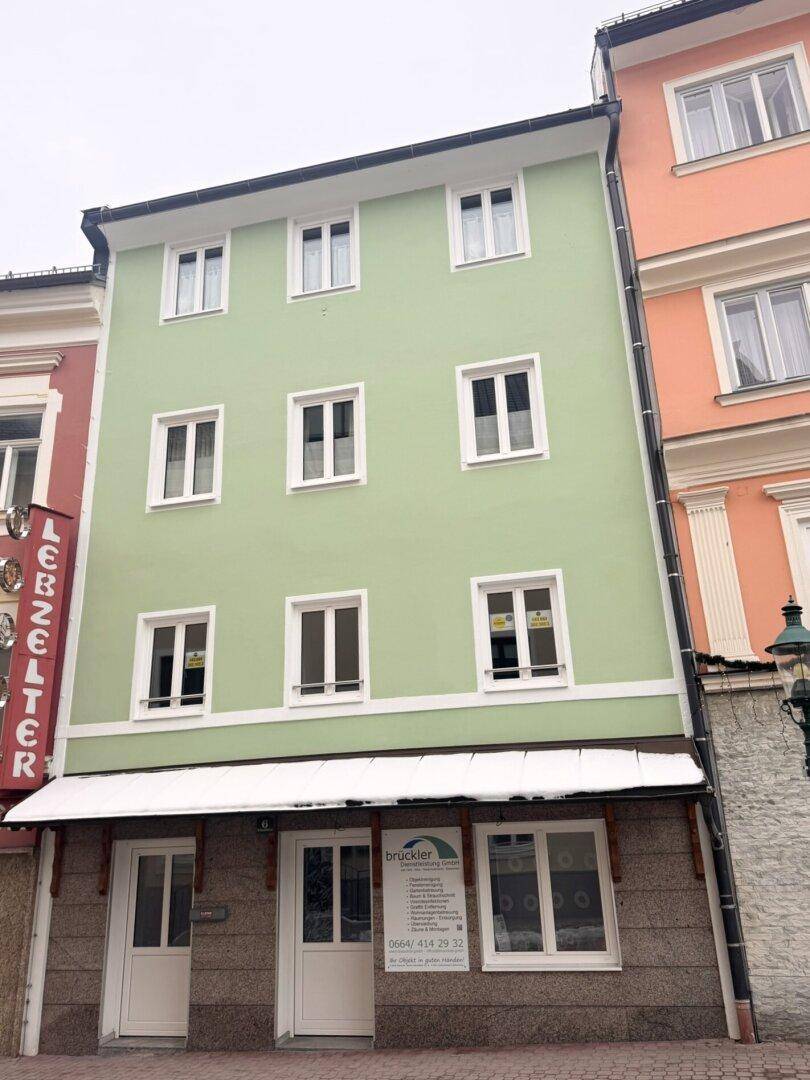 Grüne Fassade eines sanierten Mehrfamilienhauses mit mehreren weißen Fenstern und modernem Erscheinungsbild.