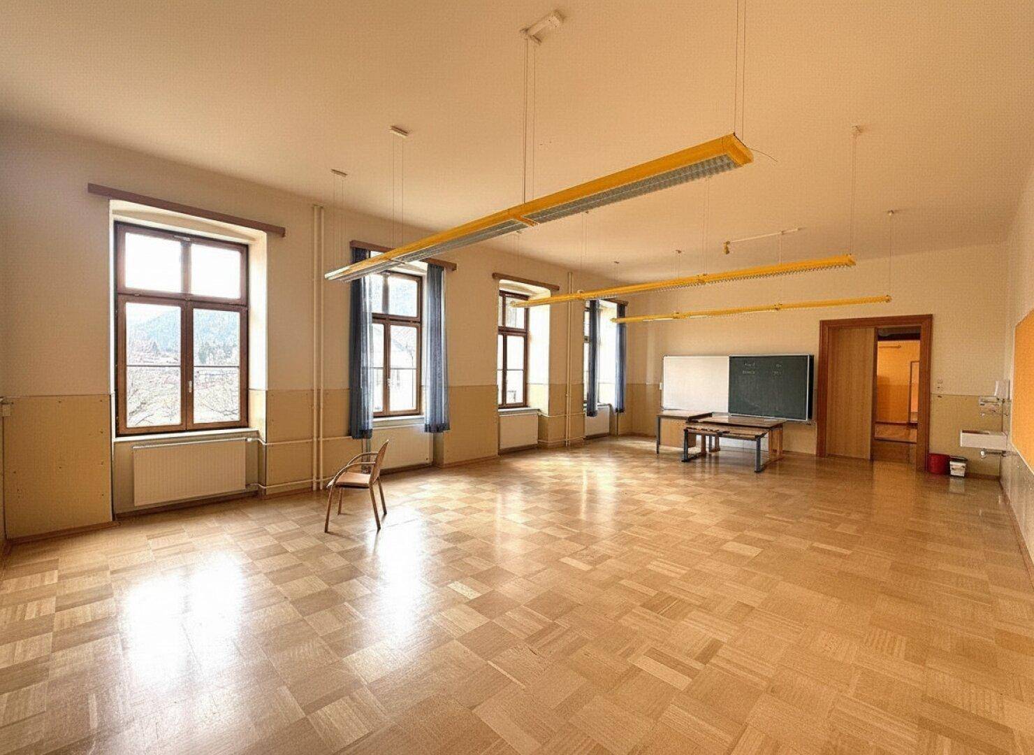 Geräumiger, heller Raum mit Fischgrätparkett, großen Fenstern und einer Tafel, ideal für Seminare.