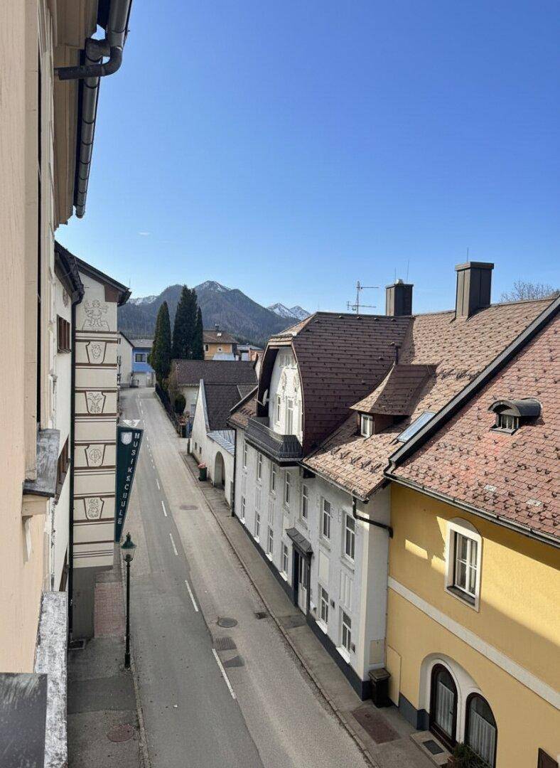 Blick auf eine ruhige Straße mit traditionellen Gebäuden und schneebedeckten Bergen im Hintergrund.