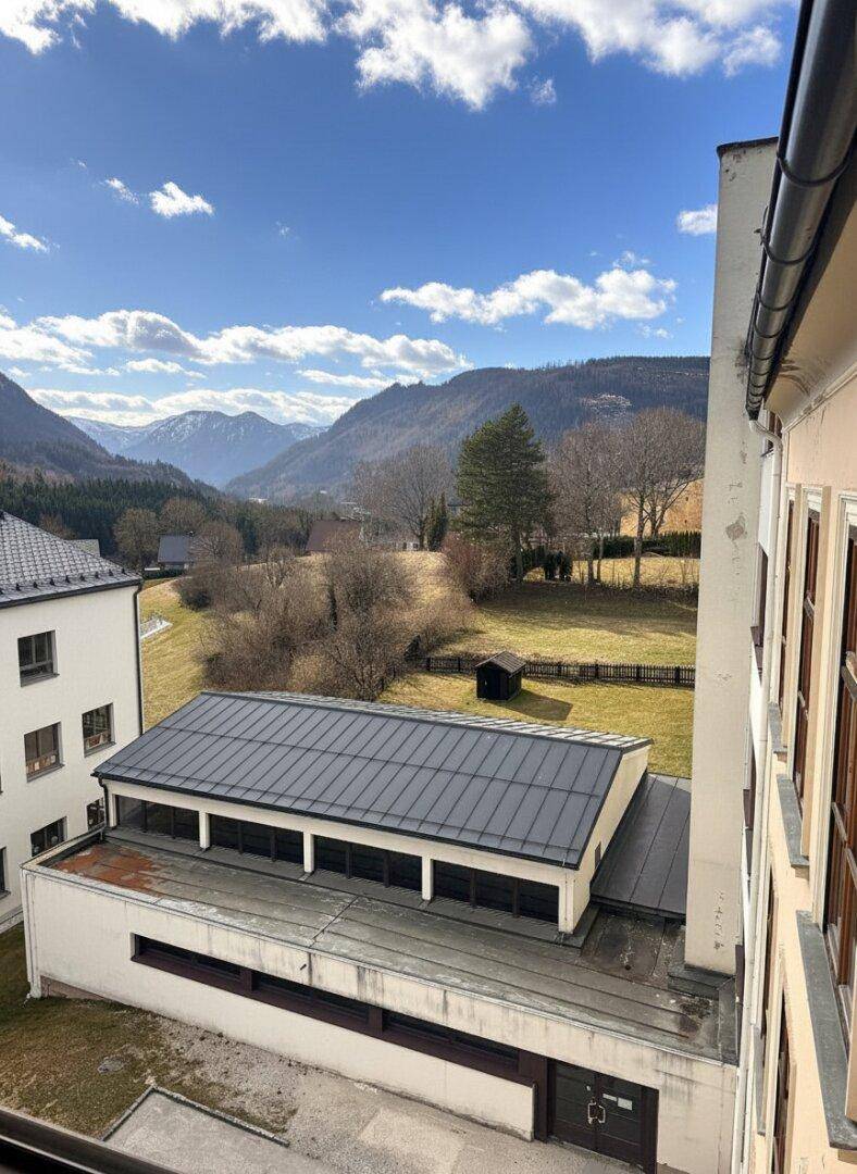 Blick aus dem Fenster auf ein Gebäude mit Flachdach und eine malerische Berglandschaft.