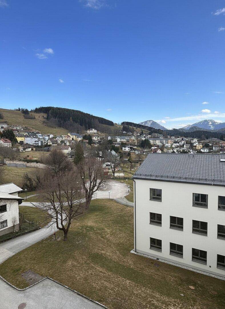 Panoramablick auf ein weißes Gebäude mit grauen Dächern und die umliegende Hügellandschaft.