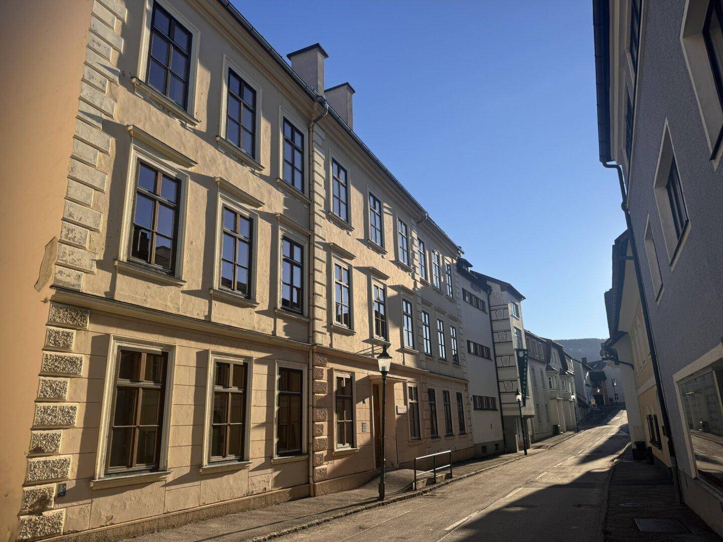 Historische Gebäude entlang einer gepflasterten Straße unter blauem Himmel.