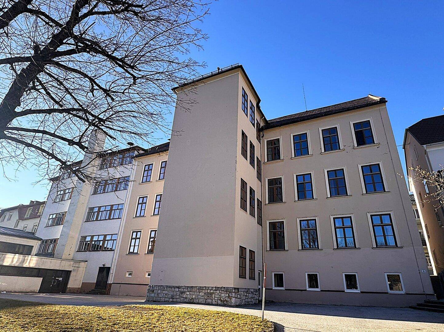 Außenansicht eines mehrstöckigen Gebäudes mit vielen Fenstern und einem Baum im Vordergrund.
