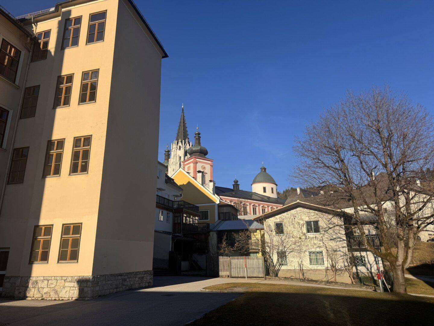 Gebäudeansicht mit einem historischen Kirchturm und einer Kuppel im Hintergrund unter klarem Himmel.