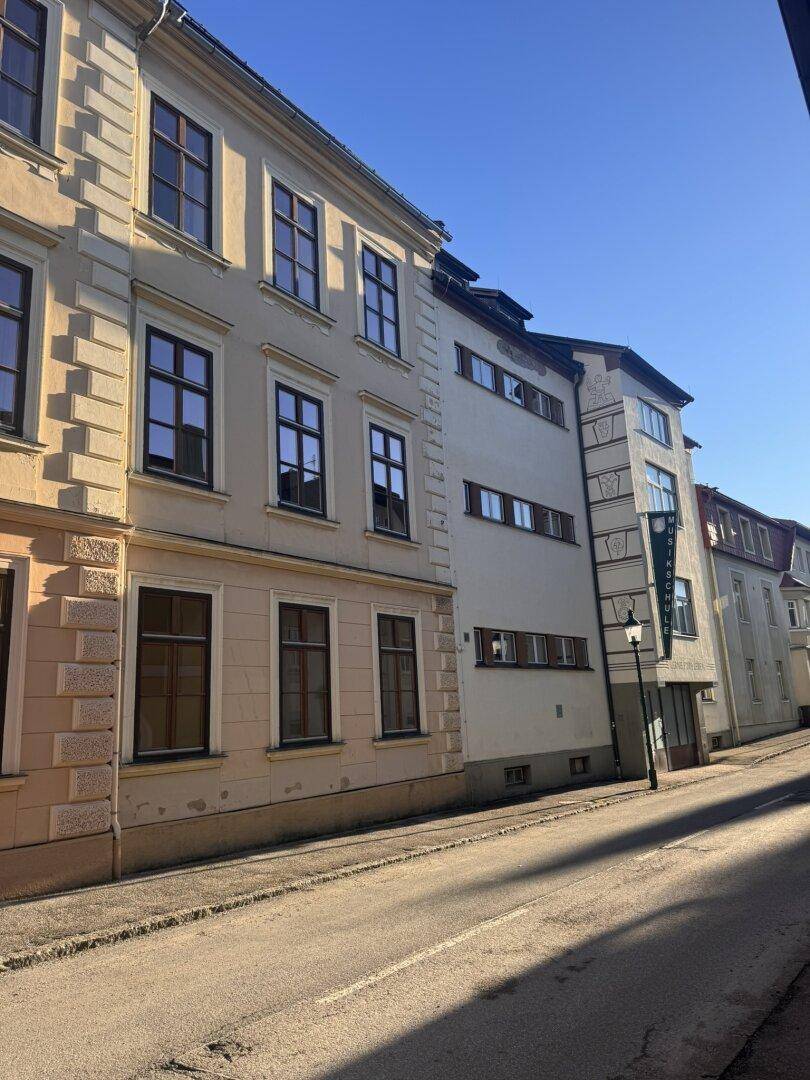 Historische Gebäude entlang einer Straße mit einer Laterne und Schattenwurf am Nachmittag.