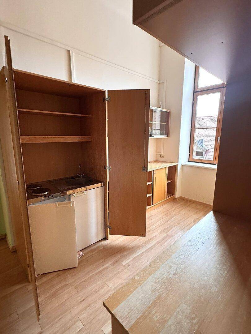 Kompakte Küchenzeile mit Kochfeld, Kühlschrank und Stauraum in einem hellen Raum mit Holzboden.