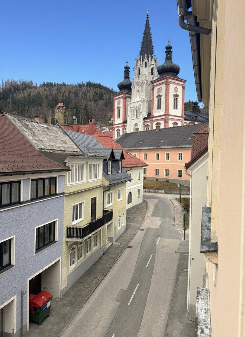 Blick auf eine historische Straße mit einer imposanten Kirche im Hintergrund unter blauem Himmel.