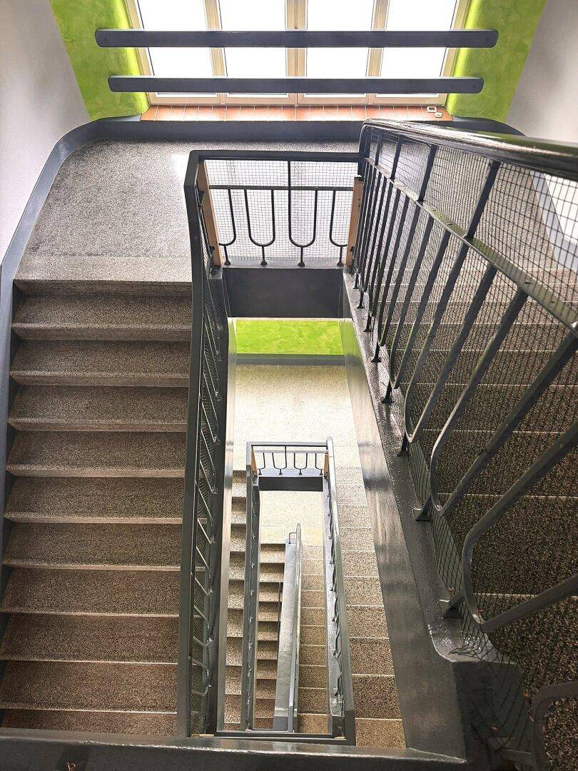 Blick von oben in ein mehrstöckiges Treppenhaus mit Terrazzostufen und Metallgeländer.