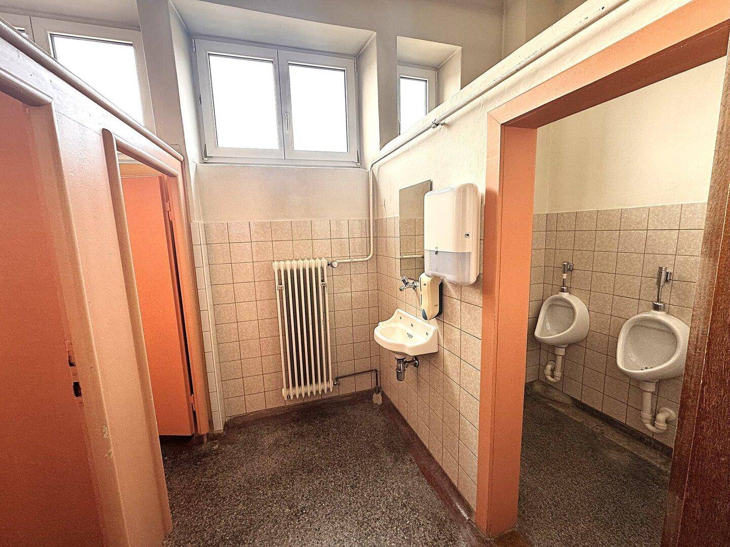 Öffentliche Toilette mit Urinalen, Waschbecken und gefliesten Wänden in Pastellfarben.