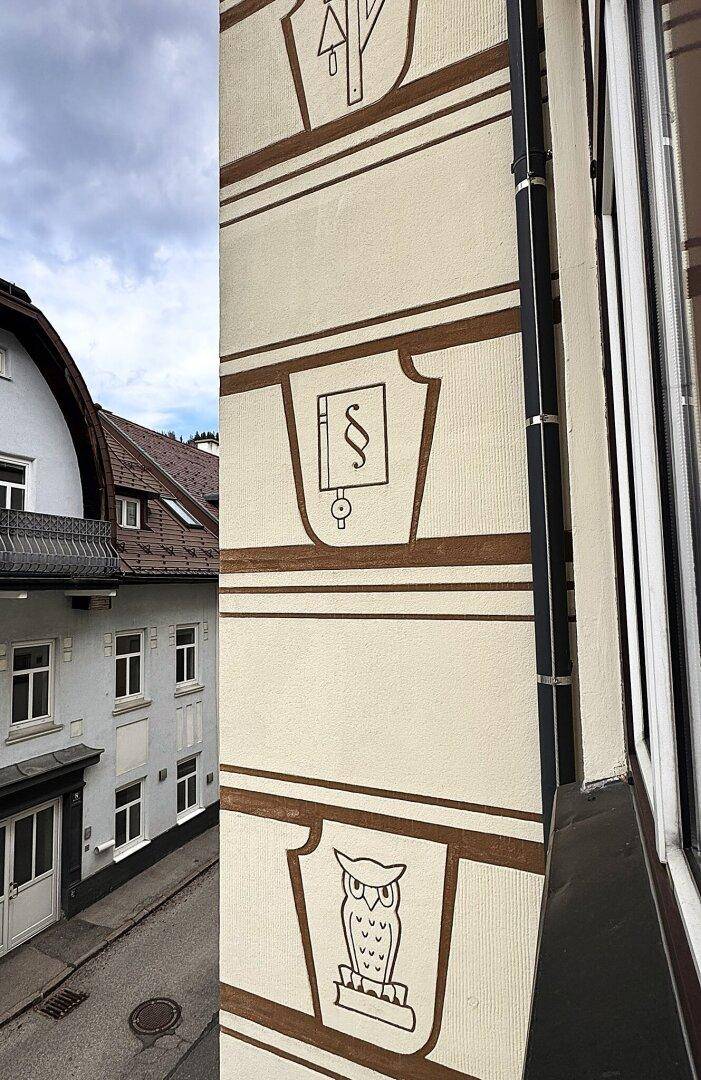 Fassadendetail eines Gebäudes mit dekorativen Symbolen und Fenstern.