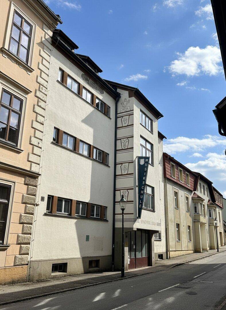 Historisches Gebäude mit 'Musikschule'-Schild an einer belebten Straße unter blauem Himmel.