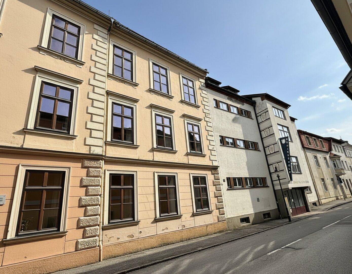 Historische Gebäude entlang einer Straße mit unterschiedlichen Fassaden und Fenstern.