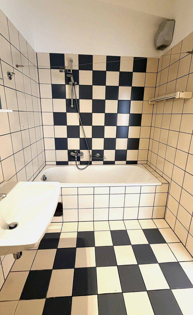 Badezimmer mit Badewanne und Waschbecken, charakterisiert durch schwarz-weiß karierte Fliesen.