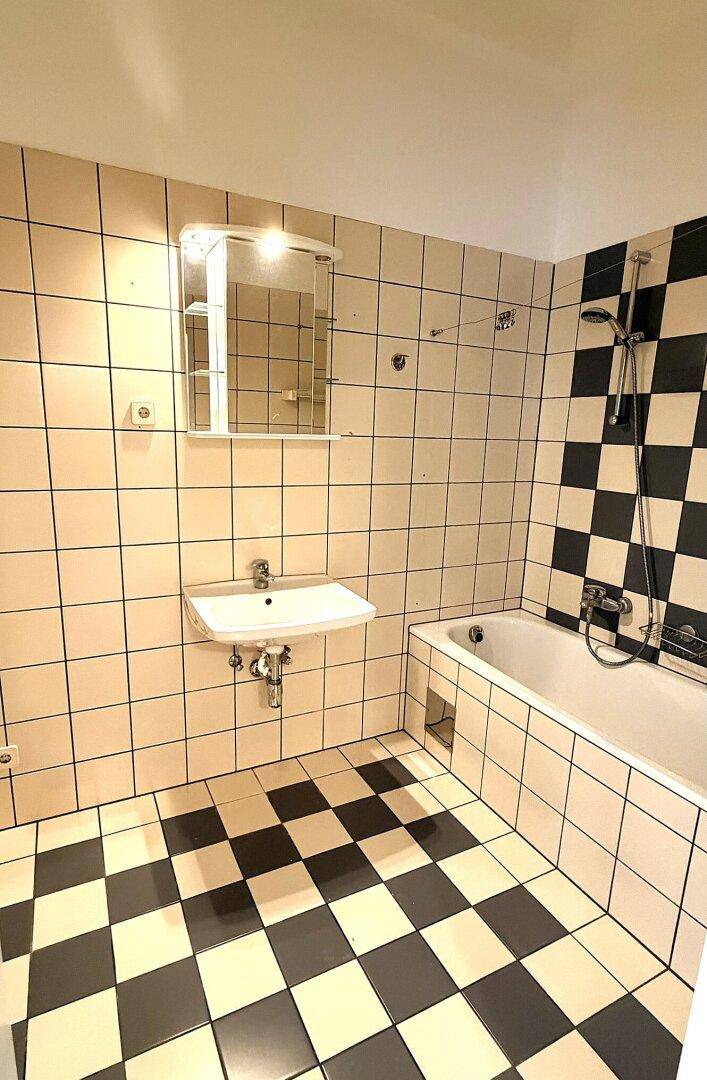 Badezimmer mit Badewanne, Waschbecken und einem Spiegelschrank über den schwarz-weiß karierten Fliesen.