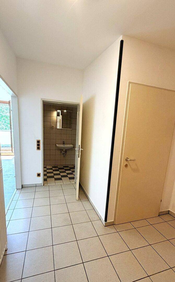 Flur mit Fliesenboden, der den Blick auf ein Badezimmer mit markanten schwarz-weiß karierten Fliesen freigibt.