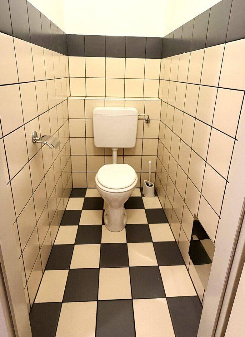 Kleines WC mit Toilette und auffälligen schwarz-weiß karierten Fliesen an Boden und Wänden.