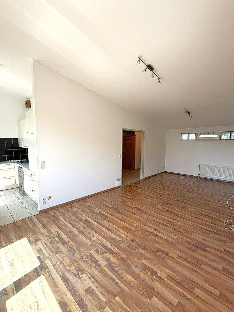 Offener Wohnbereich mit Holzboden und teilweisem Blick auf eine moderne Küche mit weißen Schränken.