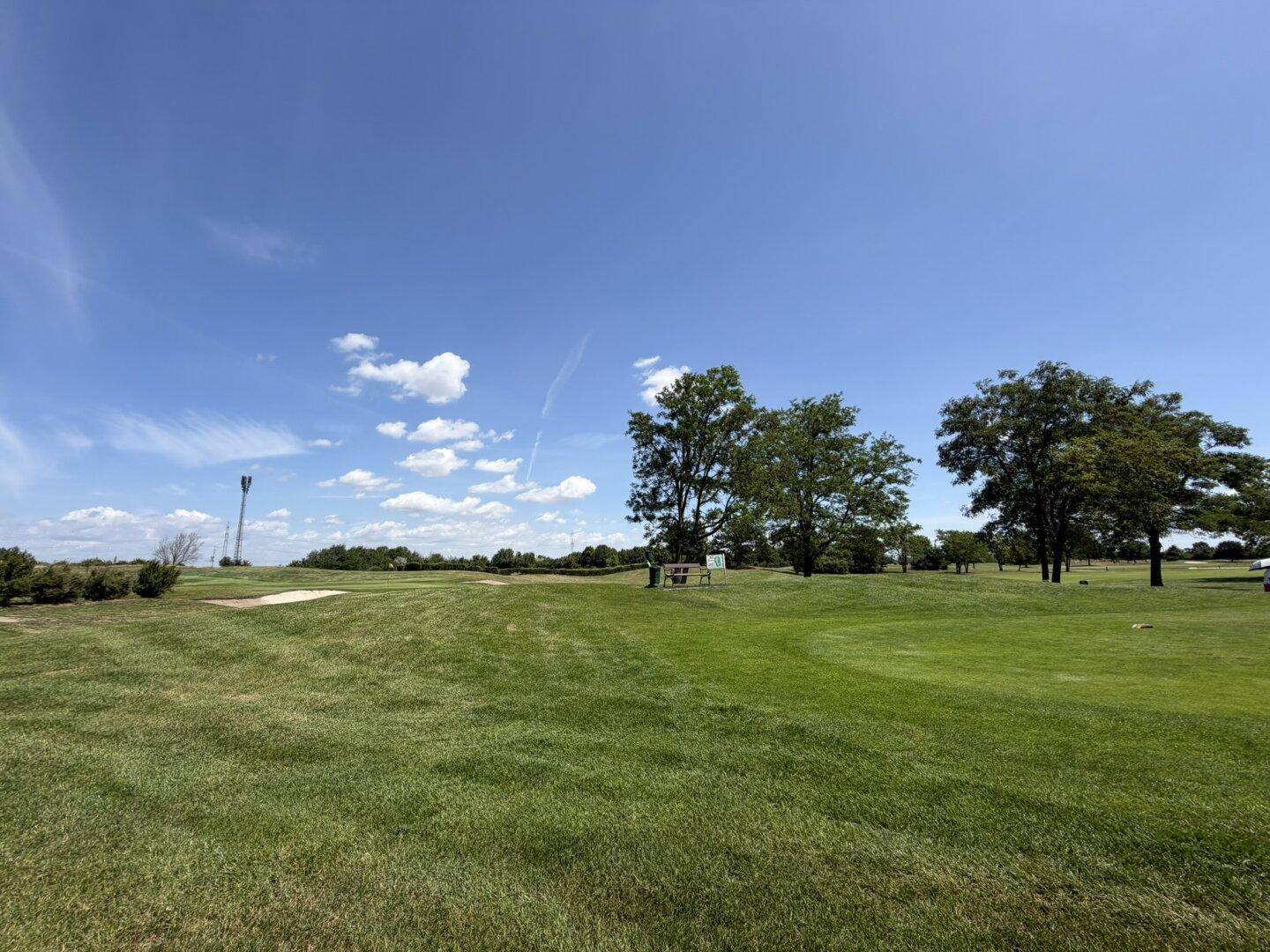 Ausgedehnter Golfplatz mit Sandbunker und einem Turm in der Ferne unter blauem Himmel.
