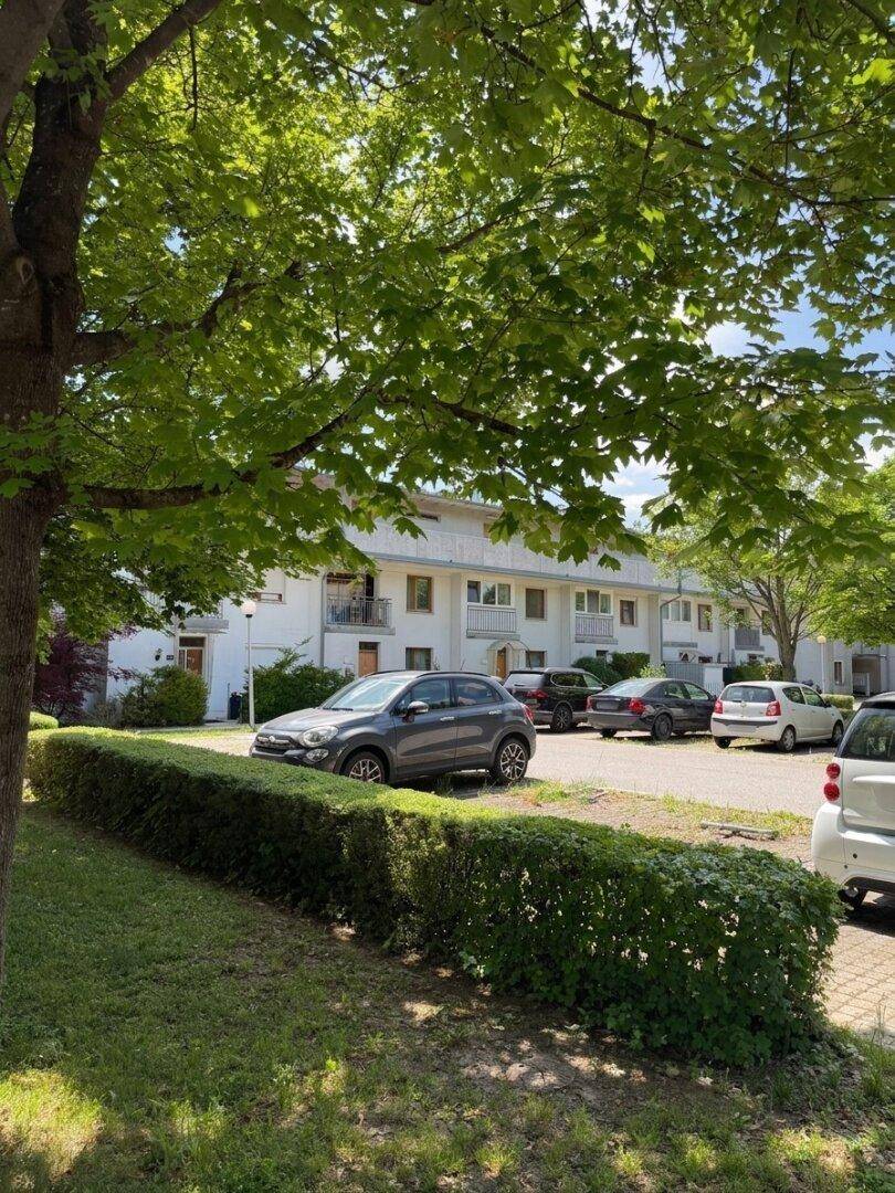 Wohngebäude mit Parkplätzen, Bäumen und Hecken im Außenbereich an einem sonnigen Tag.