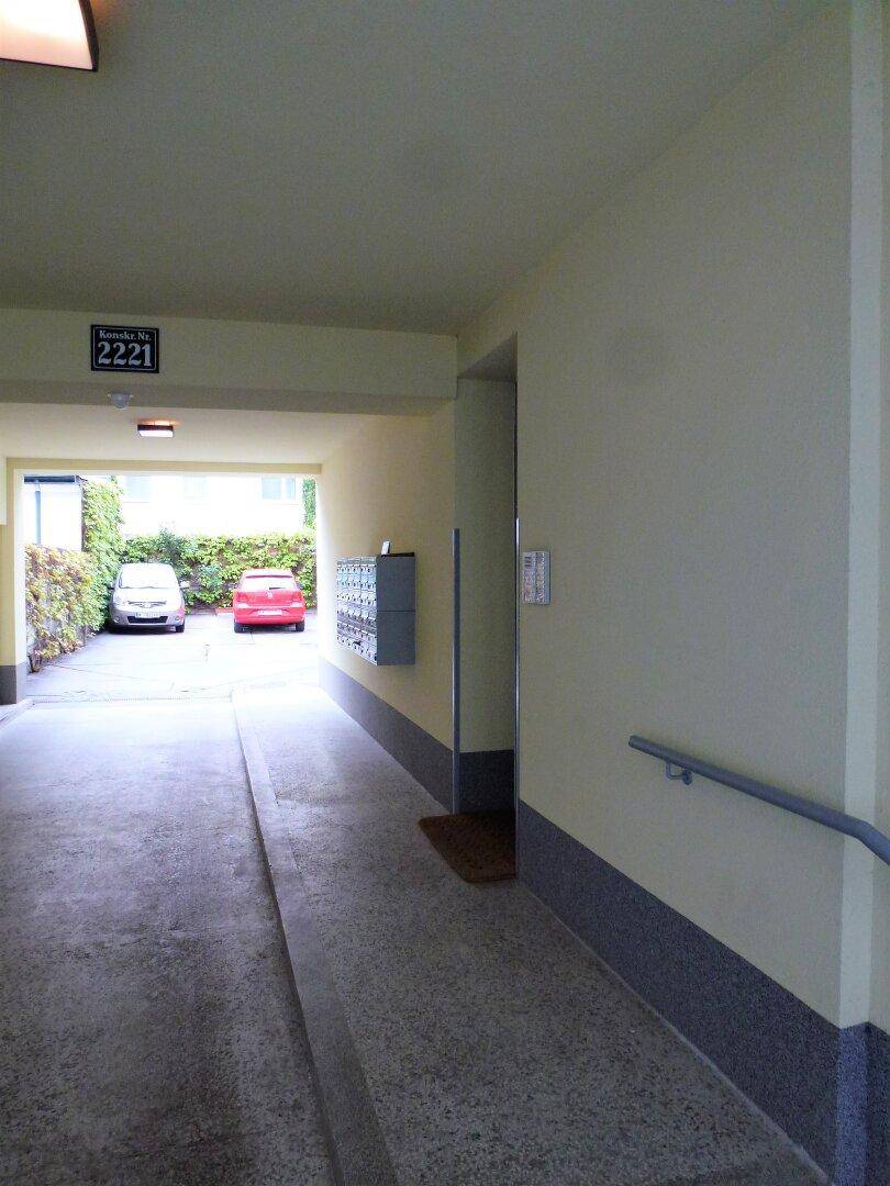 Eingangsbereich des Gebäudes mit Rampe, Briefkästen und Durchfahrt zu Parkplätzen.