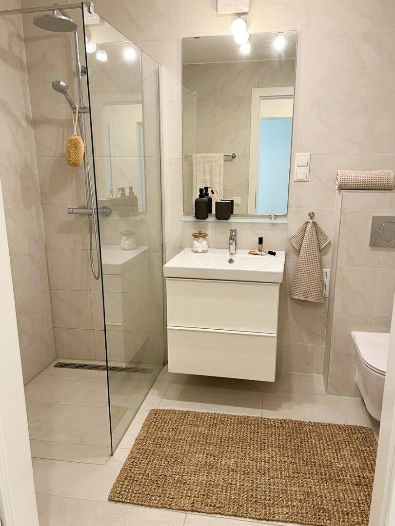 Modernes Badezimmer mit ebenerdiger Dusche, Einzelwaschbecken und hellen Fliesen.