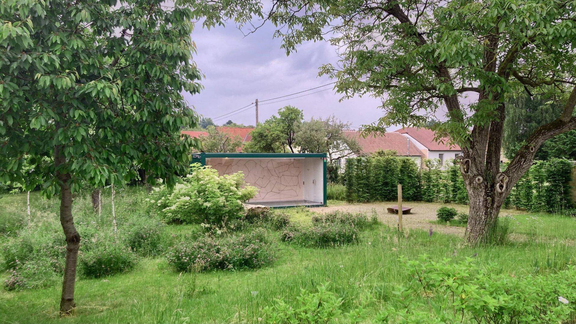 Großer, grüner Garten mit verschiedenen Bäumen und einer kleinen Gartenhütte im Hintergrund.