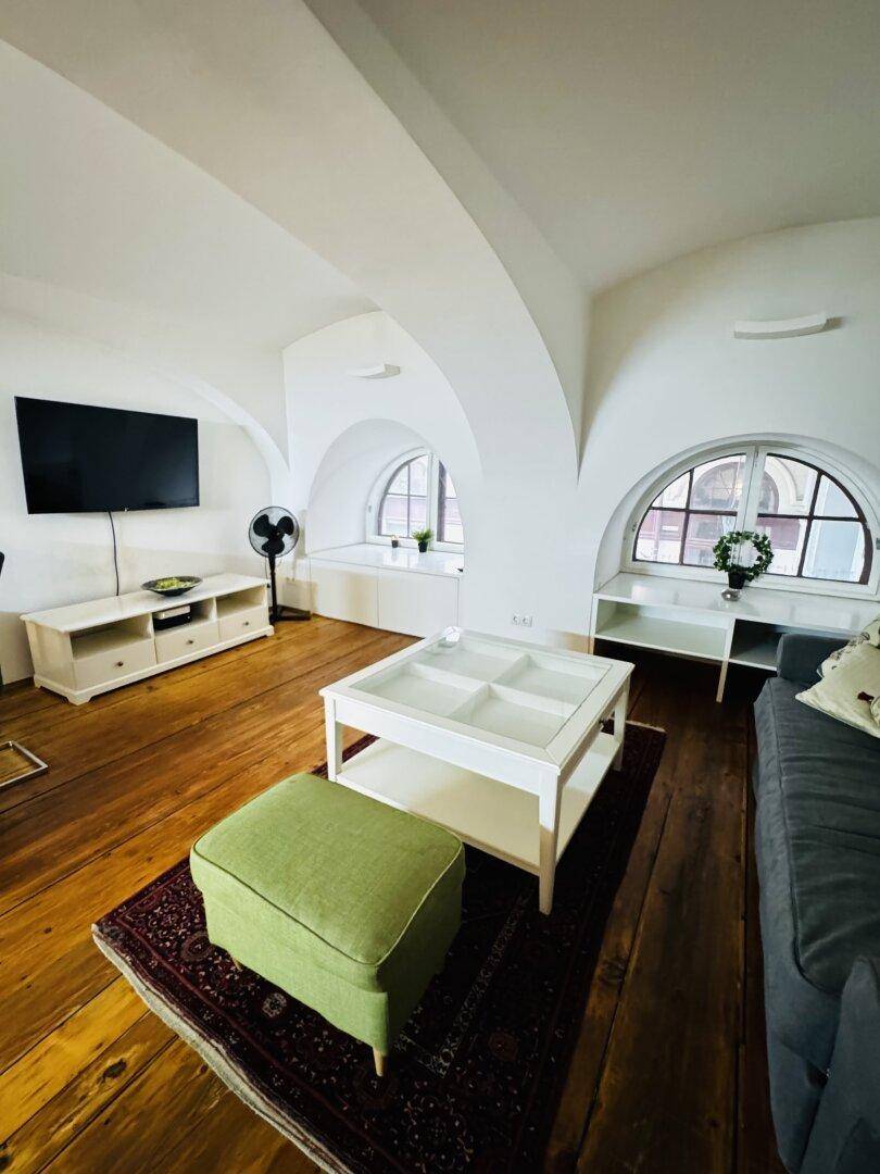 Gemütlicher Wohnbereich mit Sofa, Couchtisch, Fernseher und charakteristischen Rundbogenfenstern.