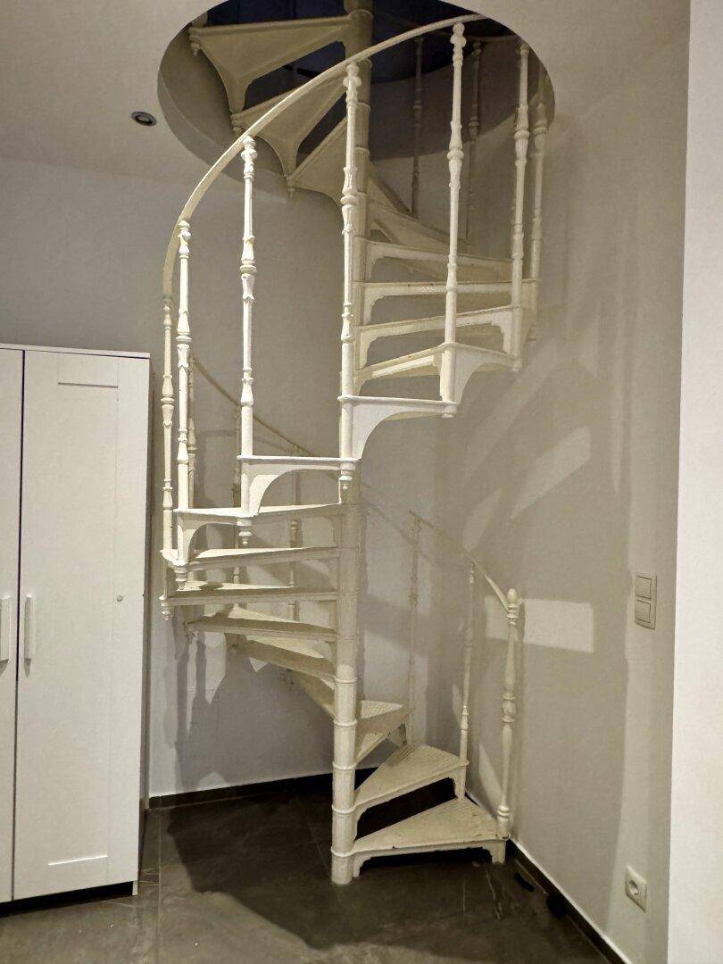 Detailaufnahme einer weißen Wendeltreppe mit filigranem Geländer.