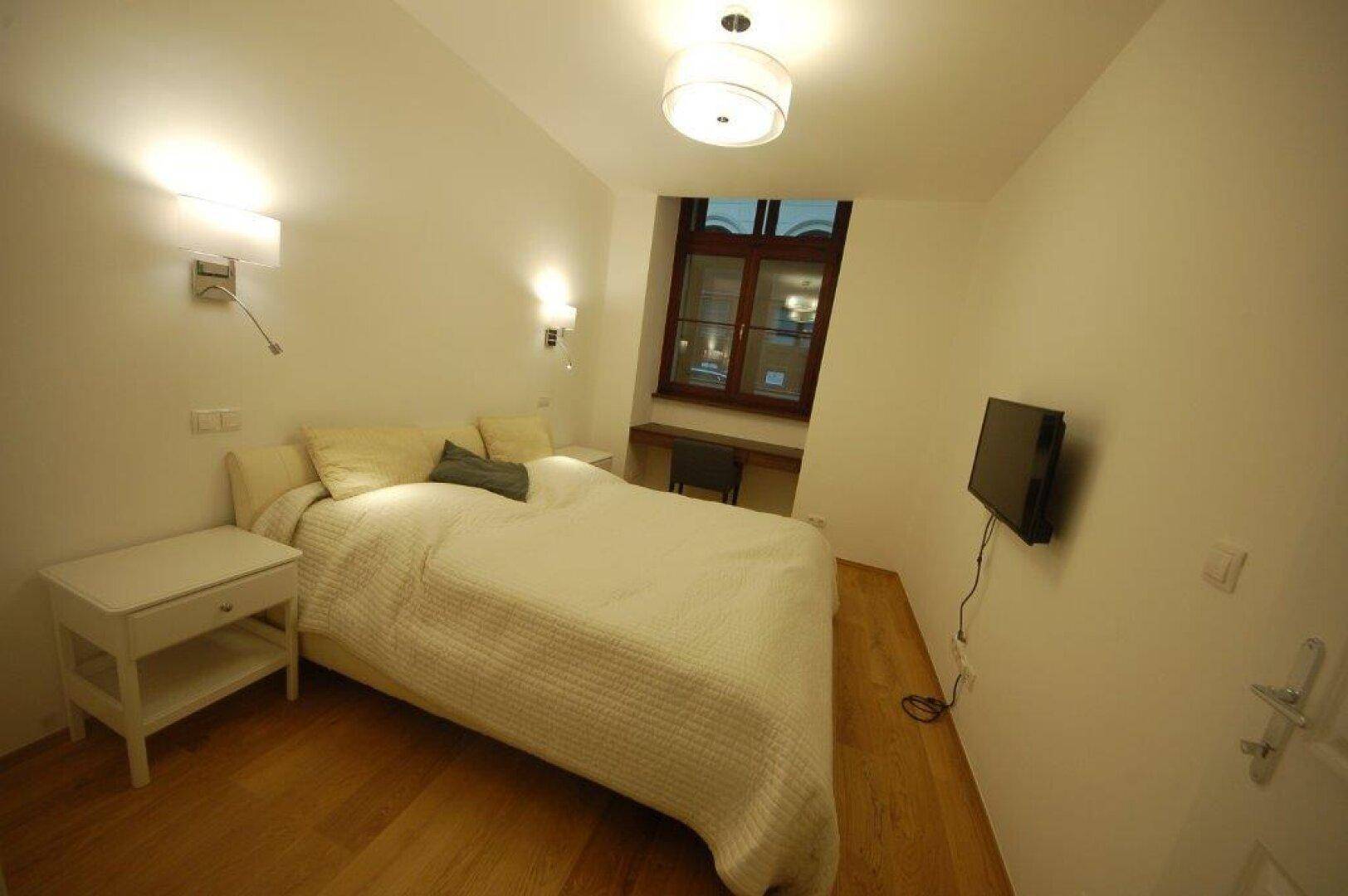 Gemütliches Schlafzimmer mit Doppelbett, Nachttisch und an der Wand montiertem Fernseher.